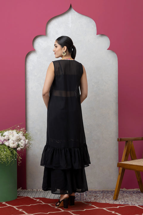 Woman in a black dress standing against a pink wall with a decorative arch.