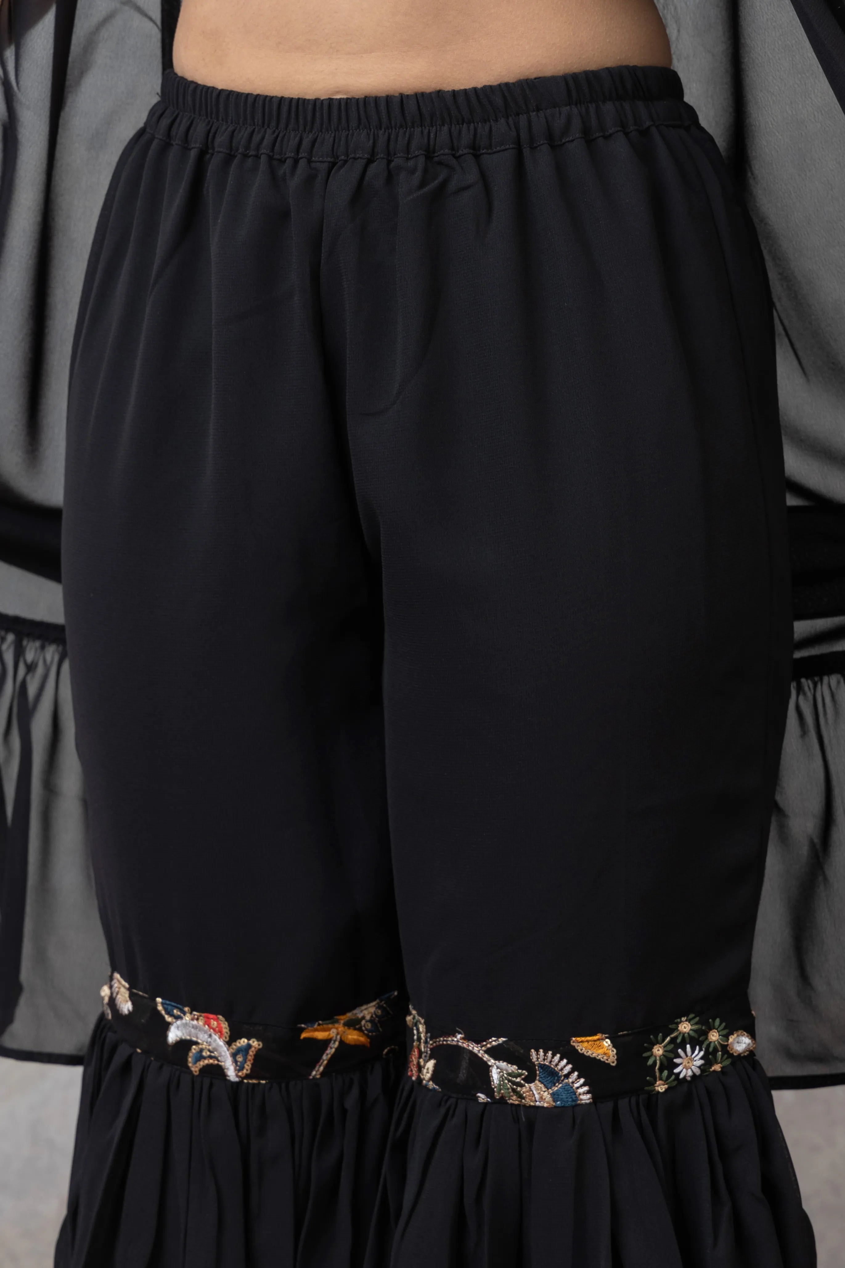 Black pants with floral embroidery at the bottom on a neutral background