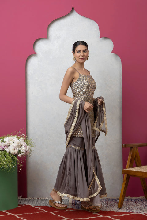 Woman in a traditional outfit standing against a pink wall with a decorative mirror.