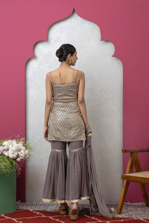 Woman in a silver top and gray pants standing against a pink wall with a decorative arch.