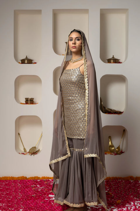 Woman in a traditional outfit with a gray dupatta against a decorative wall.