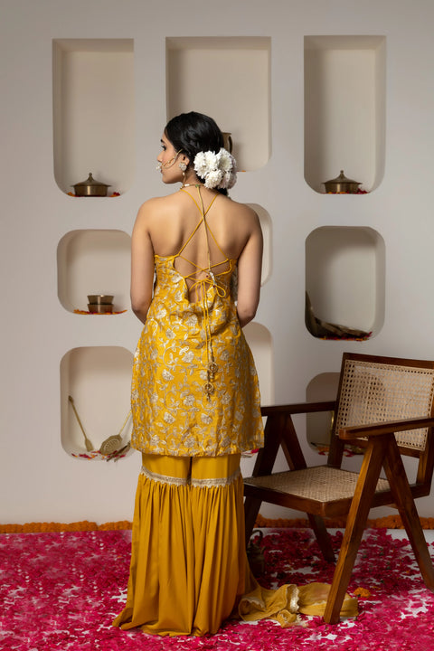Woman in a yellow floral dress standing in a room with a pink rug and wooden chair.