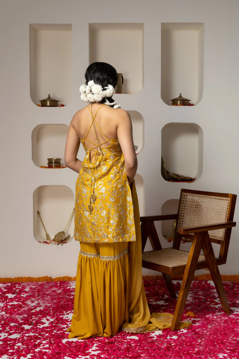 Woman in a yellow floral dress standing in a room with a wooden chair and decorative wall niches.