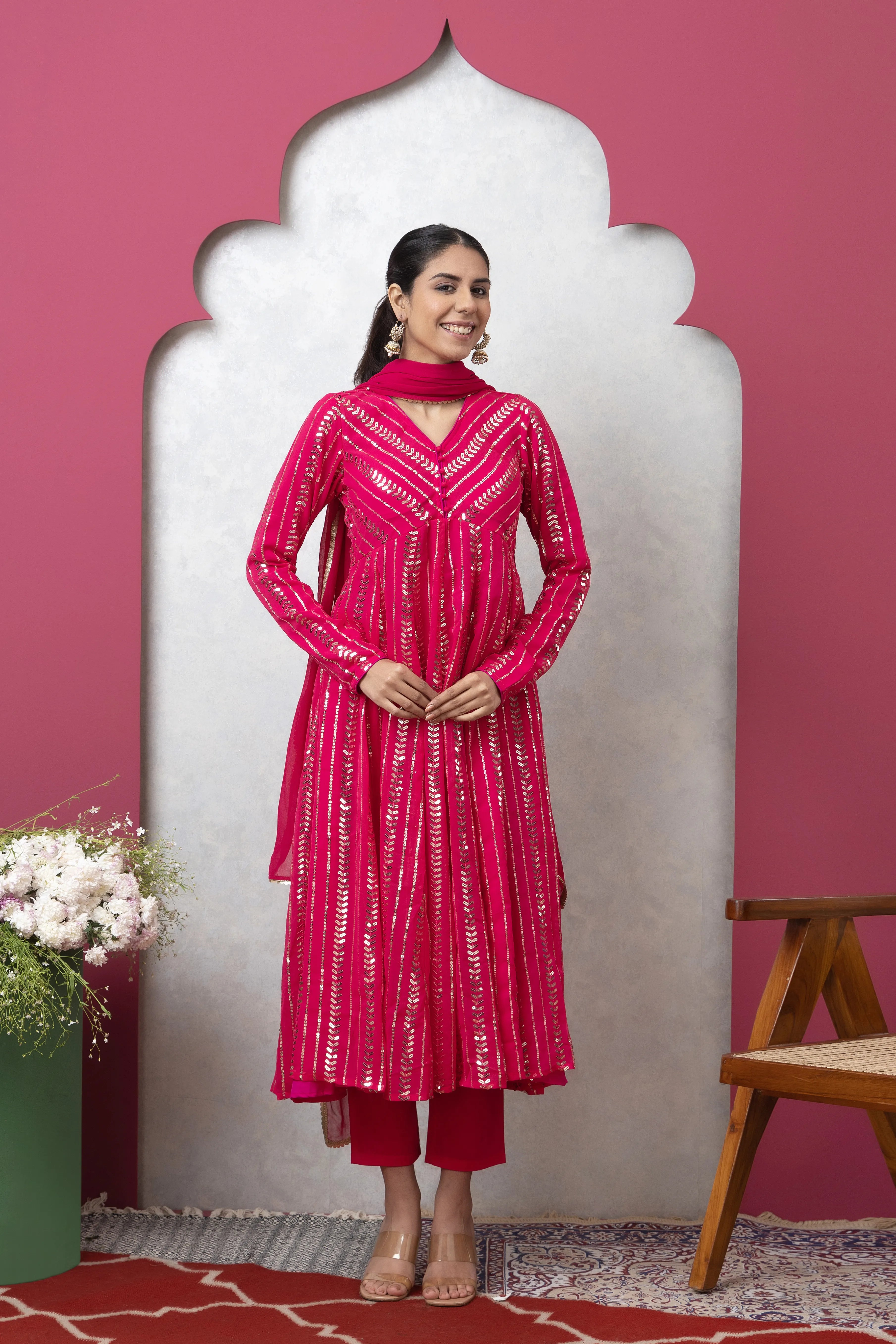 Woman in a pink traditional outfit standing against a pink wall with a decorative arch.
