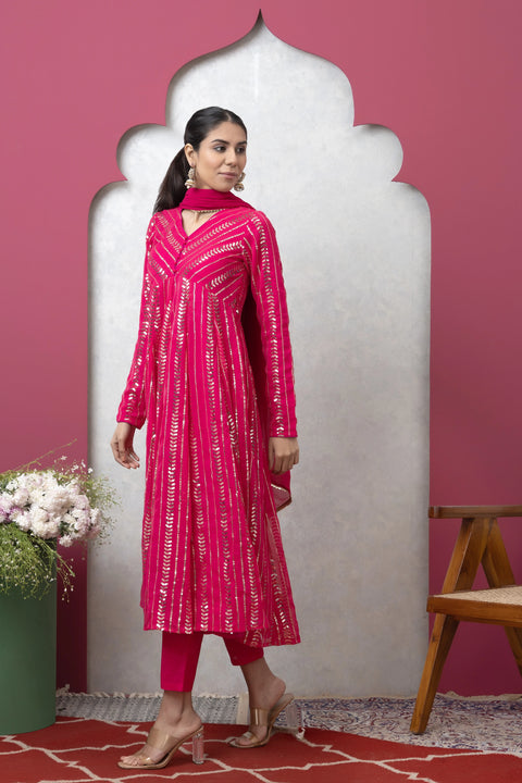 Woman in a pink traditional outfit standing against a pink wall with a white arch.