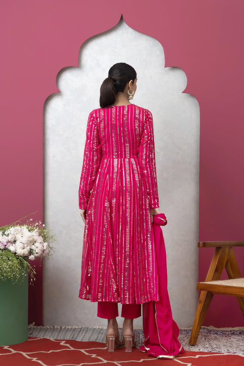 Woman in a pink traditional outfit standing in front of a decorative archway with a pink wall.