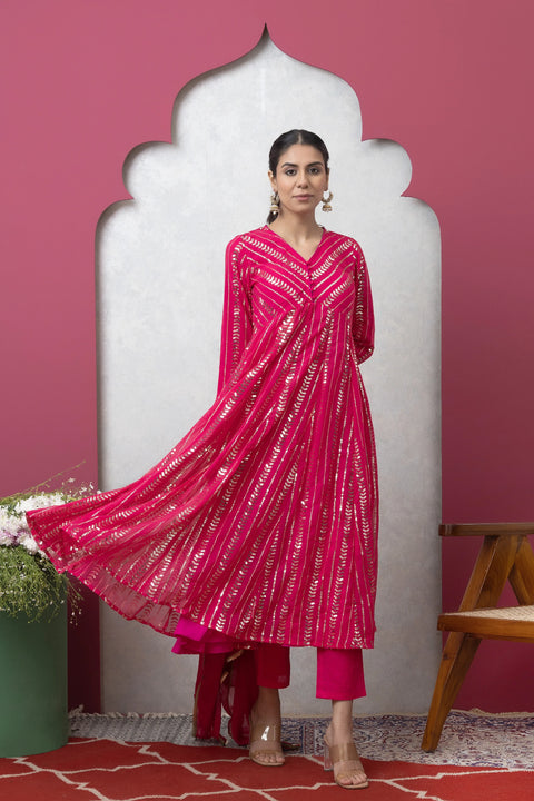 Woman wearing a pink traditional outfit with white patterns against a pink wall.