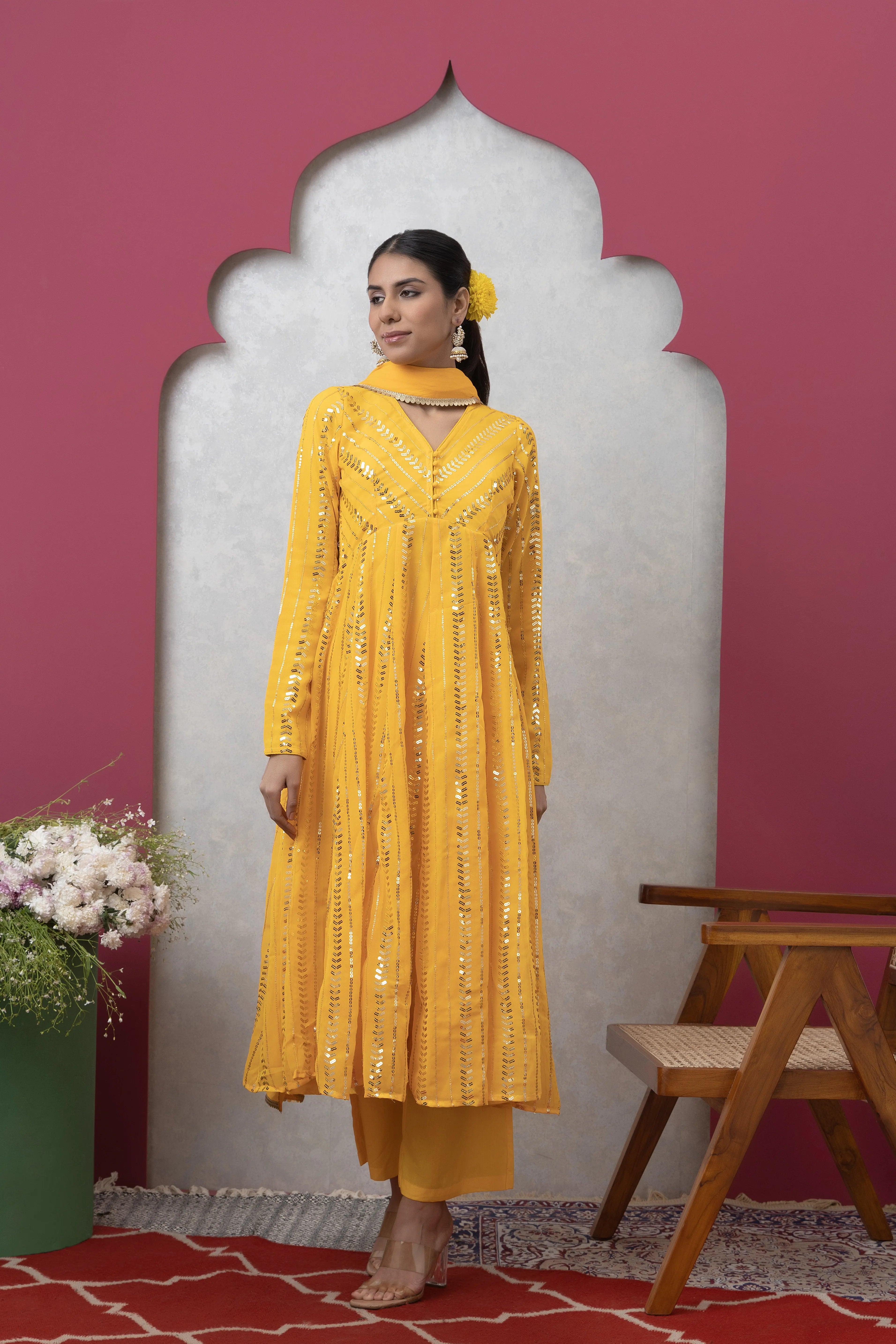 Woman in a yellow embroidered outfit standing against a pink wall with a decorative arch.
