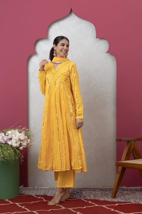 Woman in a yellow traditional outfit standing against a pink wall with a decorative arch.