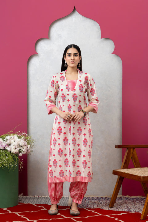 Woman wearing a white and pink floral kurta with pink pants against a pink wall.