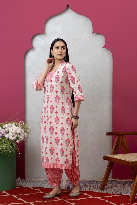 Woman wearing a pink and white floral kurta with red pants against a pink wall.