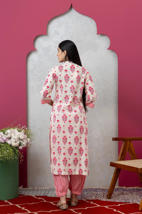Woman wearing a pink and white floral kurta with red pants against a pink wall.