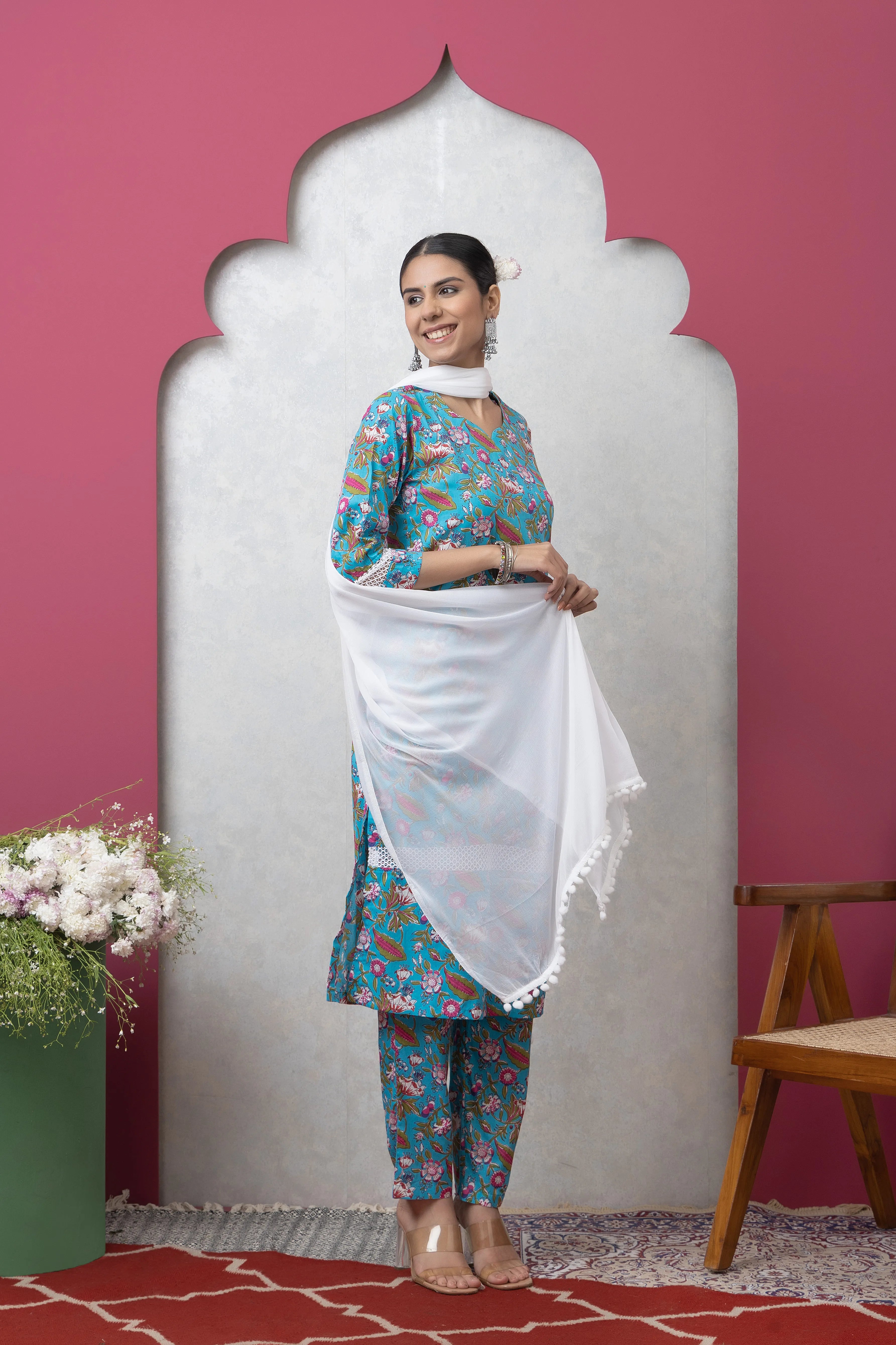 Woman in a traditional outfit with a white dupatta against a pink wall.
