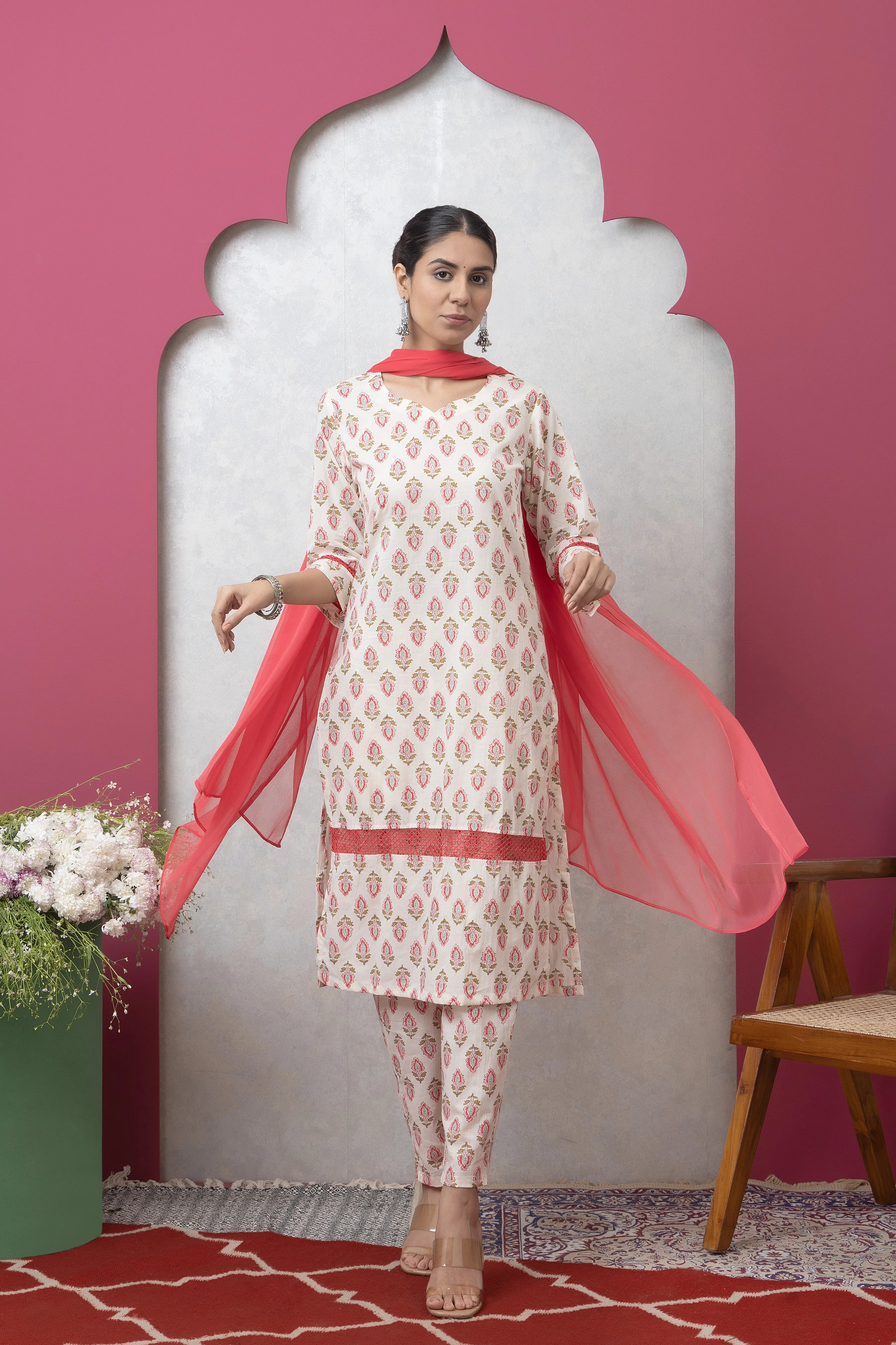 Woman wearing a traditional outfit with a pink dupatta against a pink wall.