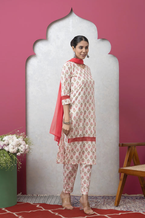 Woman in a patterned outfit with a red scarf standing against a pink wall.
