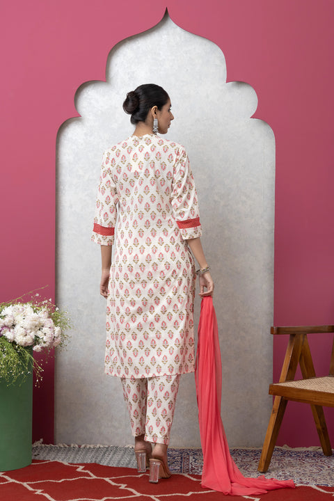 Woman in a white and red patterned kurta with pants holding a pink dupatta against a pink wall.