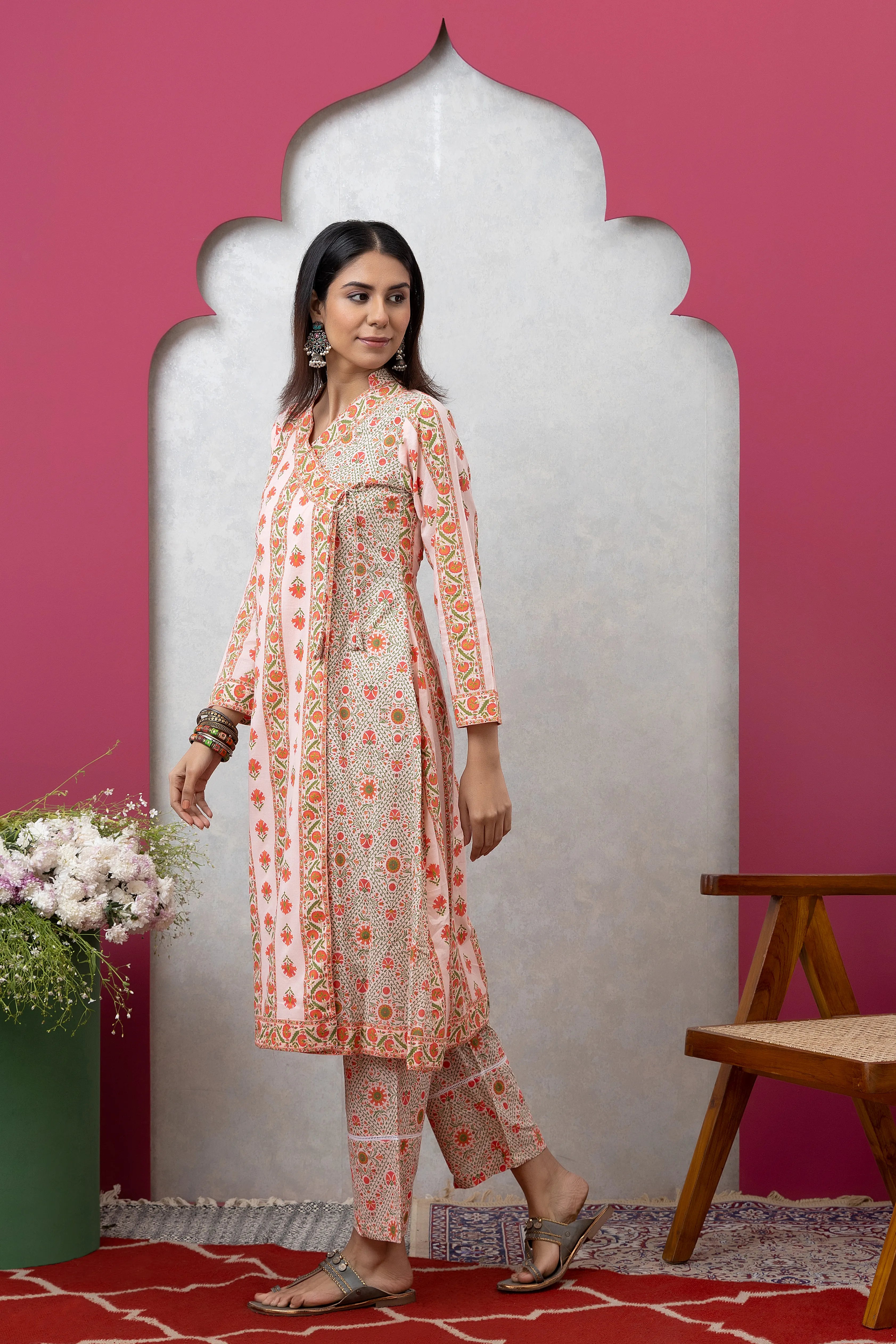 Woman in a floral kurta standing against a pink wall with a decorative arch.