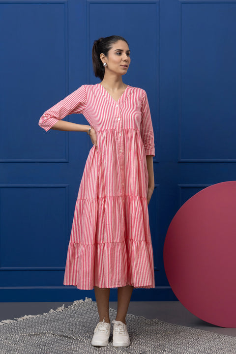 Woman wearing a pink and white striped dress against a blue wall.