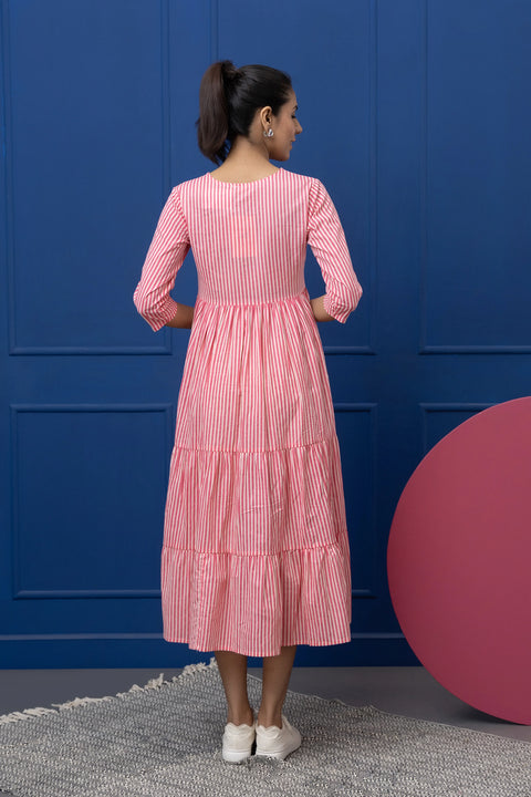 Woman wearing a pink and white striped dress against a blue wall.