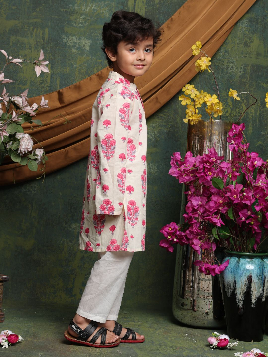 Child wearing a floral outfit standing in front of decorative flowers and a mirror.
