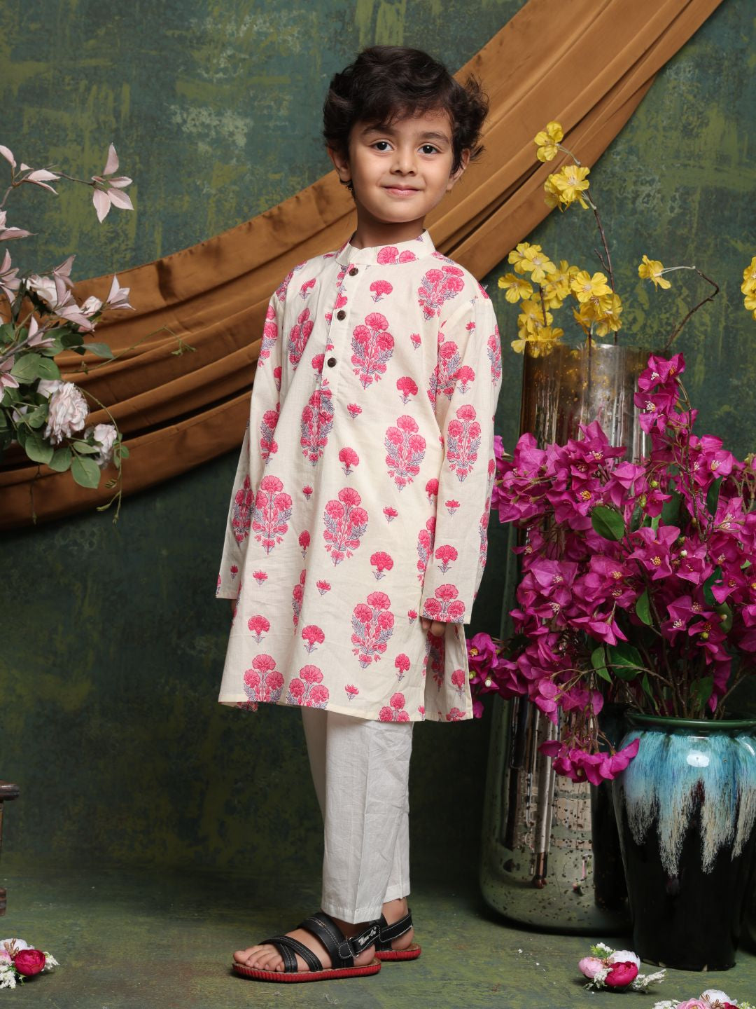 Child wearing a floral outfit standing in front of decorative flowers and a wooden frame.