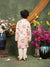 Child wearing a colorful floral outfit standing in front of a mirror with flowers on a green textured wall.