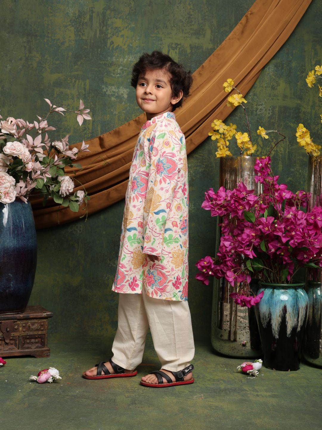 Child wearing a floral outfit standing in front of decorative flowers and a mirror.