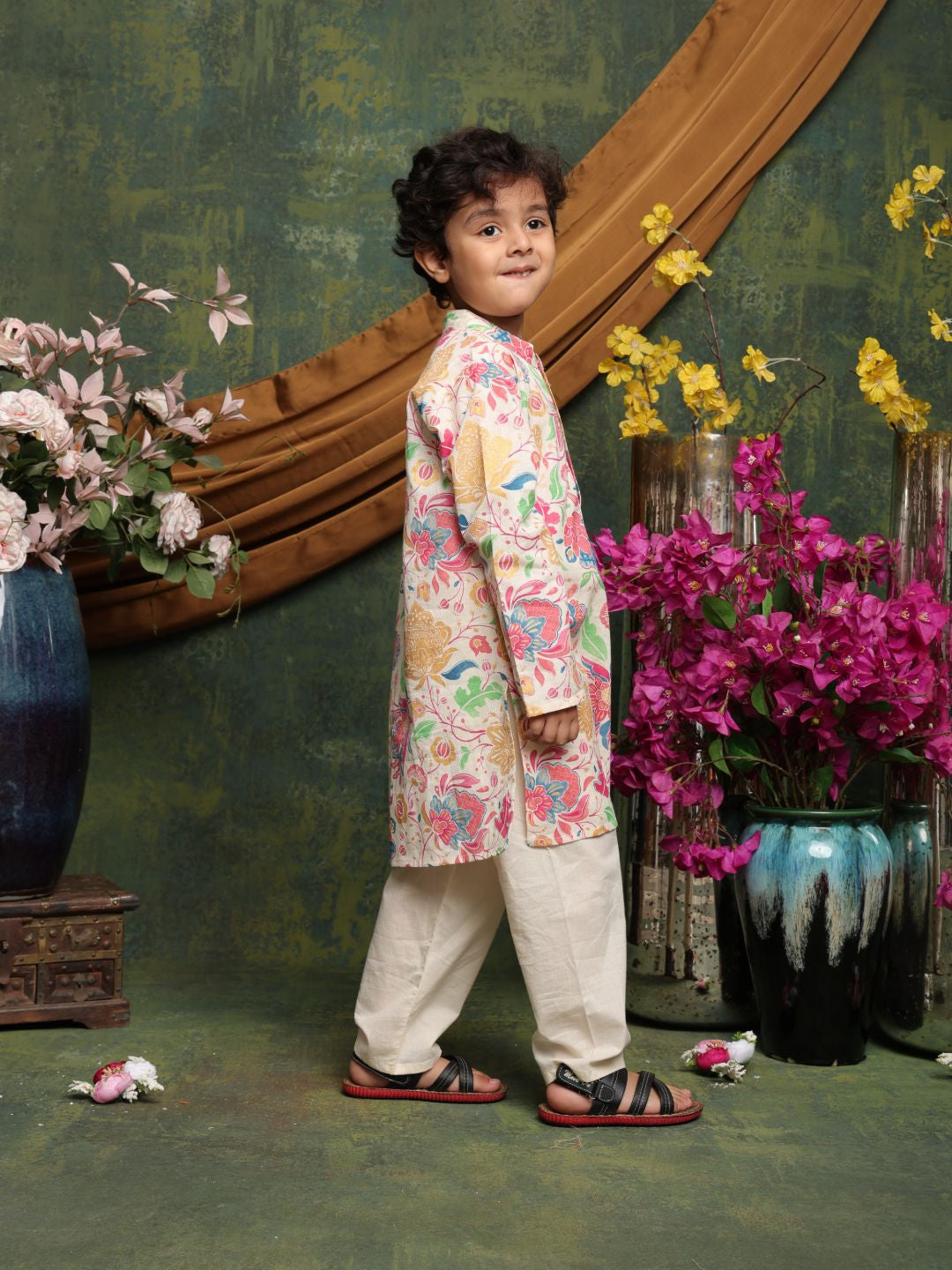 Child wearing a floral kurta with a decorative background featuring flowers and a mirror.