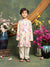 Child wearing a floral kurta with white pants standing in front of decorative flowers and vases.
