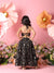 Woman in a black patterned dress standing in front of large flowers on a pink background