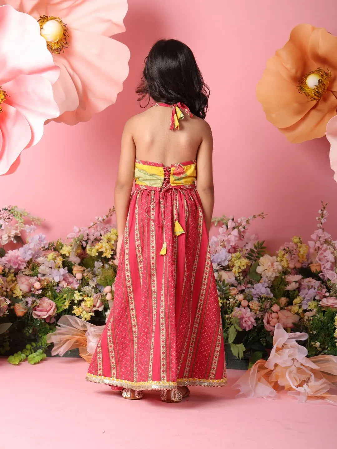 Woman in a red and yellow dress standing in front of a floral backdrop with large flowers.