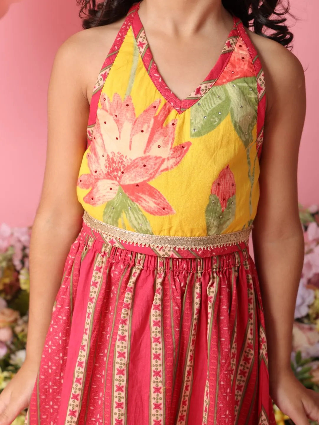 Woman wearing a colorful dress with floral top and pink skirt against a pink background