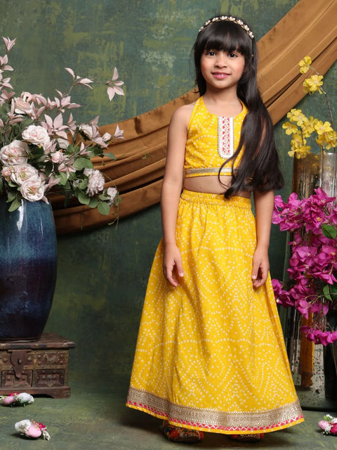 Young girl in a yellow traditional outfit standing among flowers and decorative elements.
