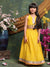 Young girl in a yellow traditional outfit standing among flowers and decorative elements.