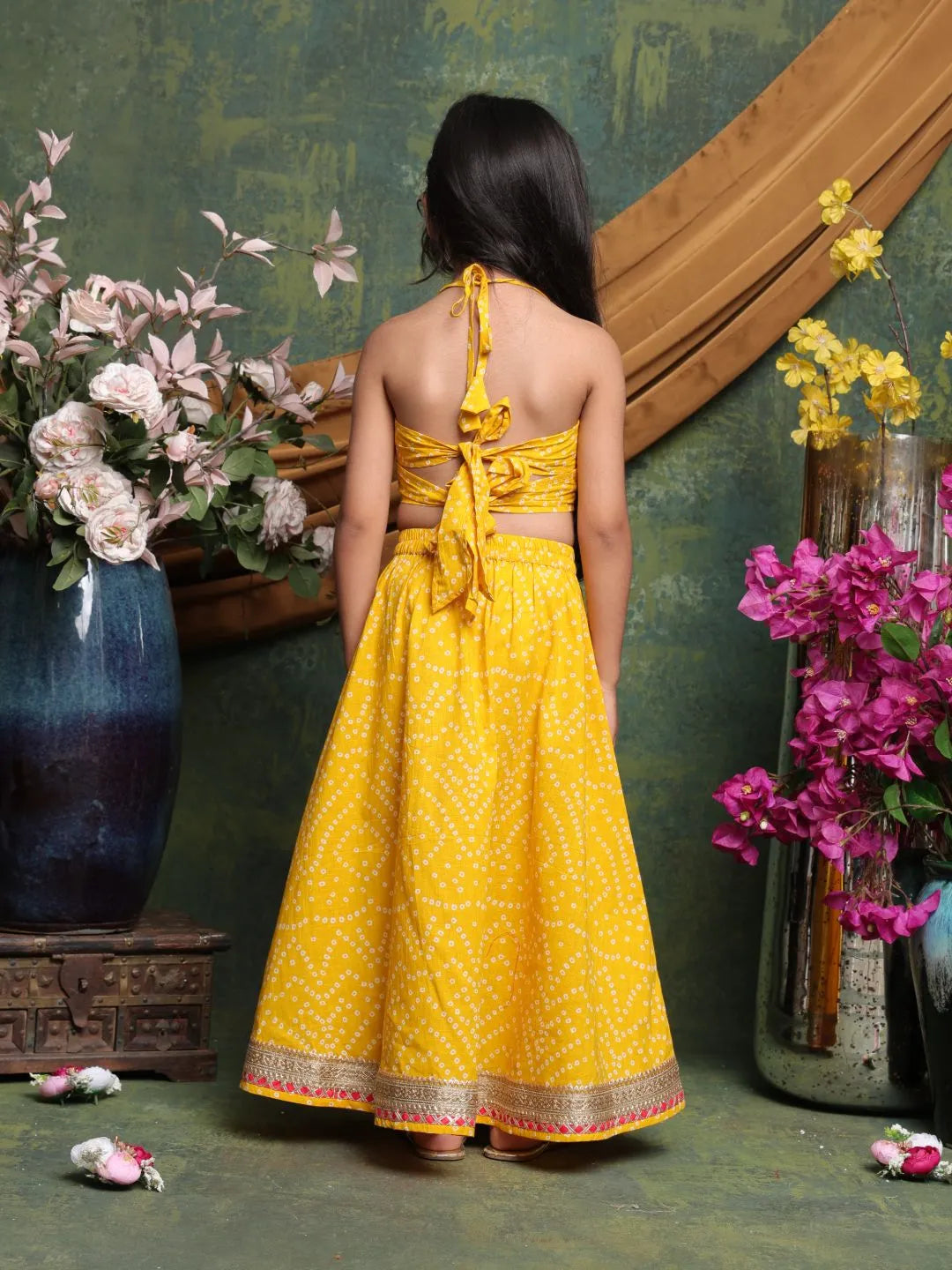 Woman wearing a yellow dress with floral decorations in a decorative setting.