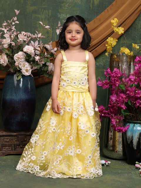 Young girl in a yellow floral dress standing in front of decorative flowers and vases.