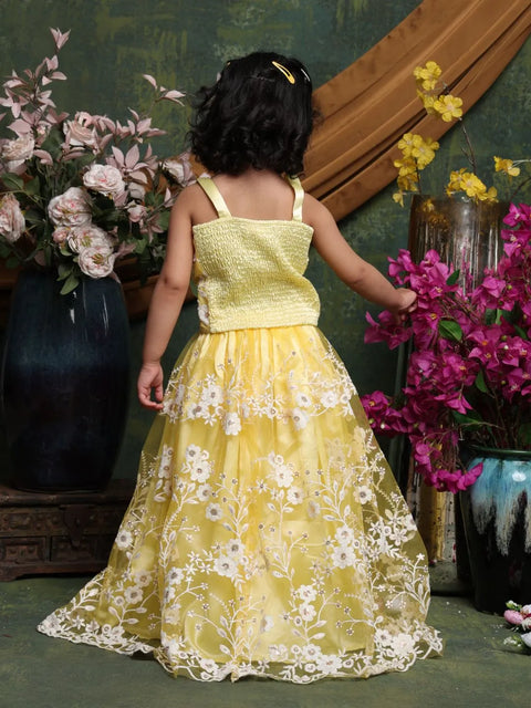 Child in a yellow floral dress standing in front of decorative flowers and vases.