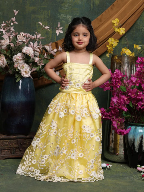 Young girl in a yellow floral dress standing in front of decorative flowers and vases.