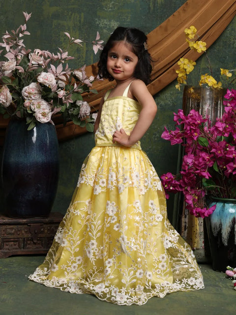 Young girl in a yellow floral dress standing among flowers and decorative elements.