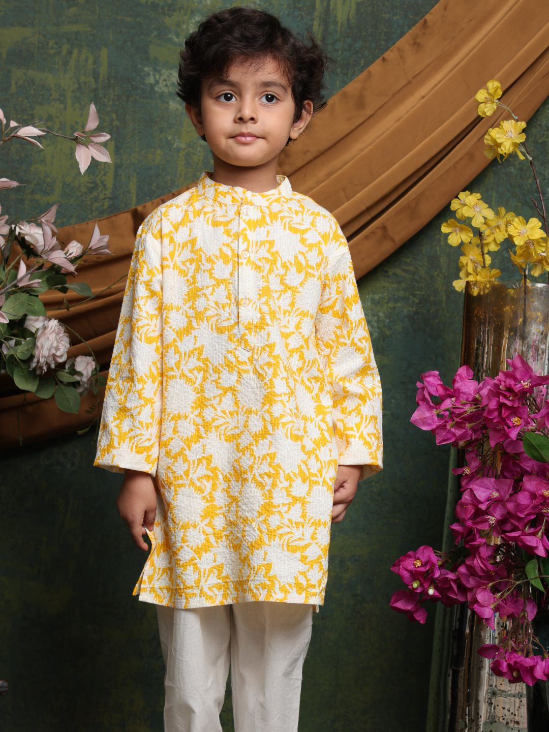 Child wearing a yellow and white floral kurta with flowers and a wooden panel in the background