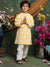 Child wearing a yellow and white traditional outfit with floral decorations and flowers in the background.