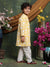 Child wearing a yellow and white floral kurta with white pants, standing in front of decorative flowers.