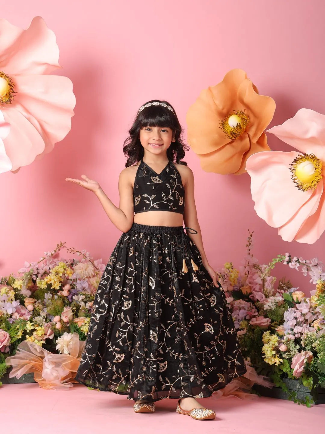 Young girl in a black embroidered outfit standing among large flowers on a pink background