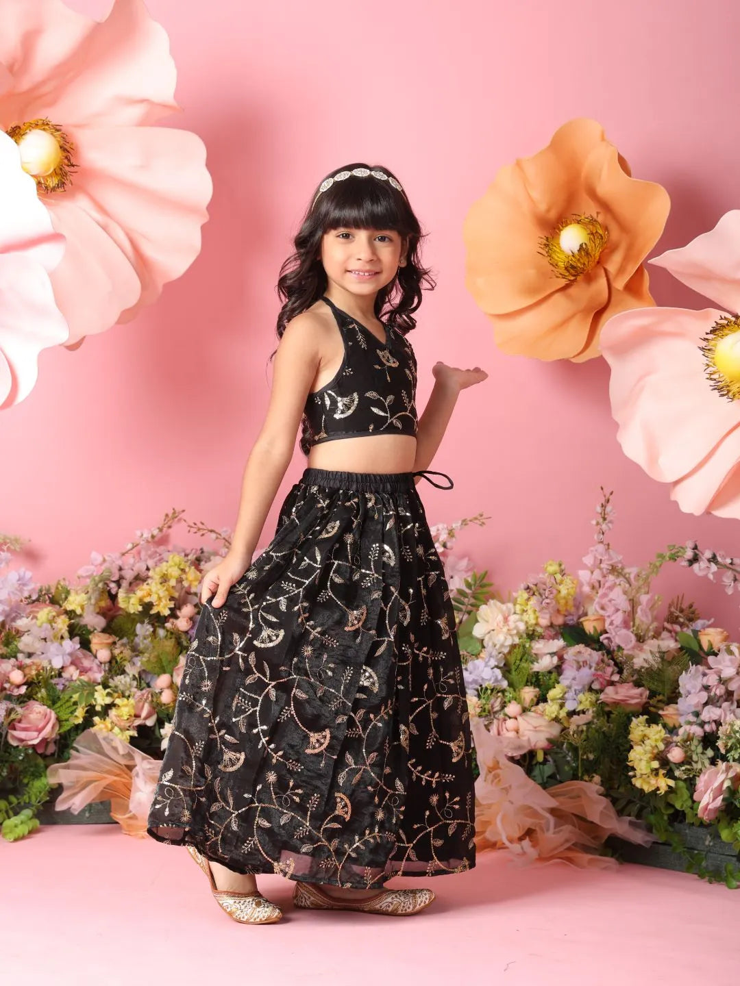 Young girl in a black floral dress standing against a pink floral backdrop