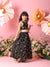 Young girl in a black floral dress standing against a pink floral backdrop