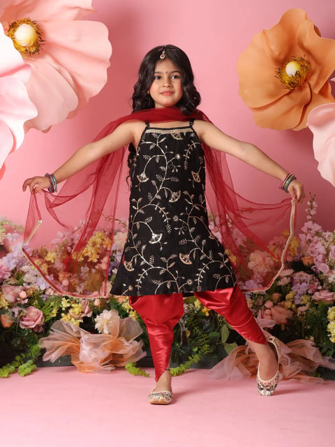 Young girl in a black floral top and red pants posing against a floral and pink background