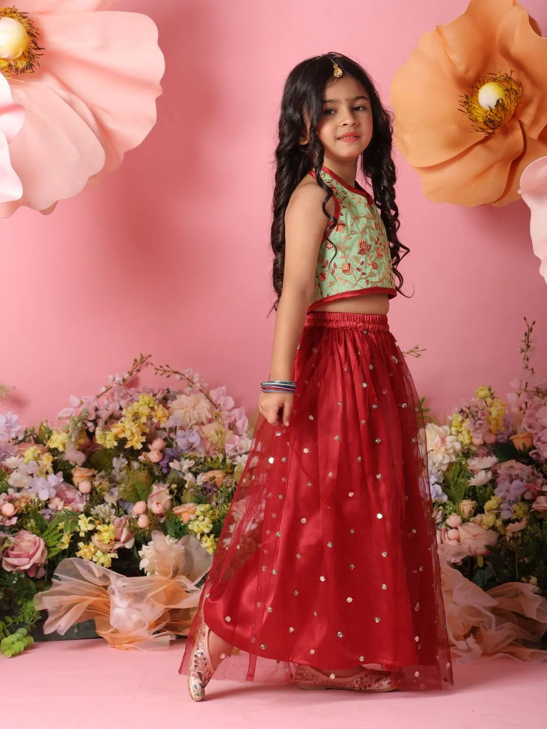 Young girl in a green top and red skirt standing in front of pink flowers