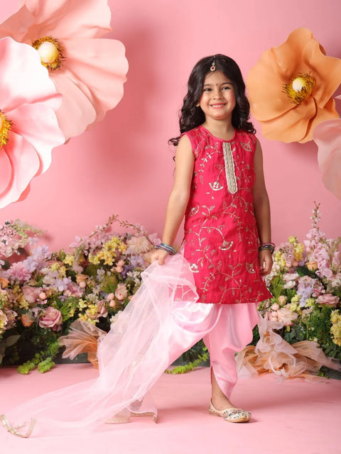 Young girl in a pink traditional outfit standing against a floral backdrop with a pink background