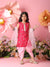 Young girl in a pink traditional outfit standing against a floral backdrop with pink flowers.