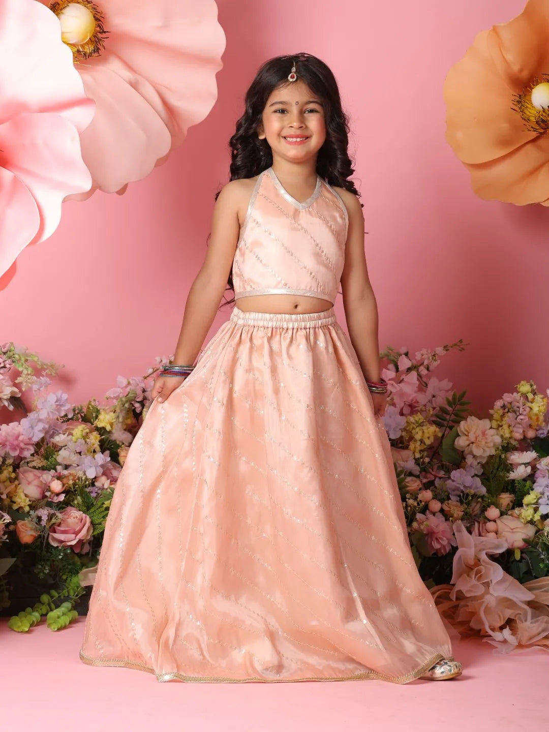 Young girl in a pink traditional outfit standing against a pink background with flowers.